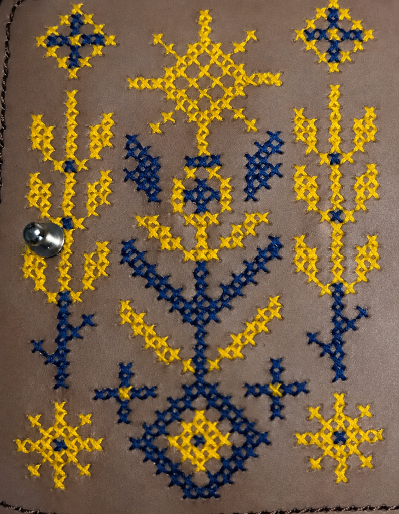 Hand-embroidered Ukrainian Guardian of Abundance symbol on leather, featuring traditional motifs of prosperity, growth and protection.